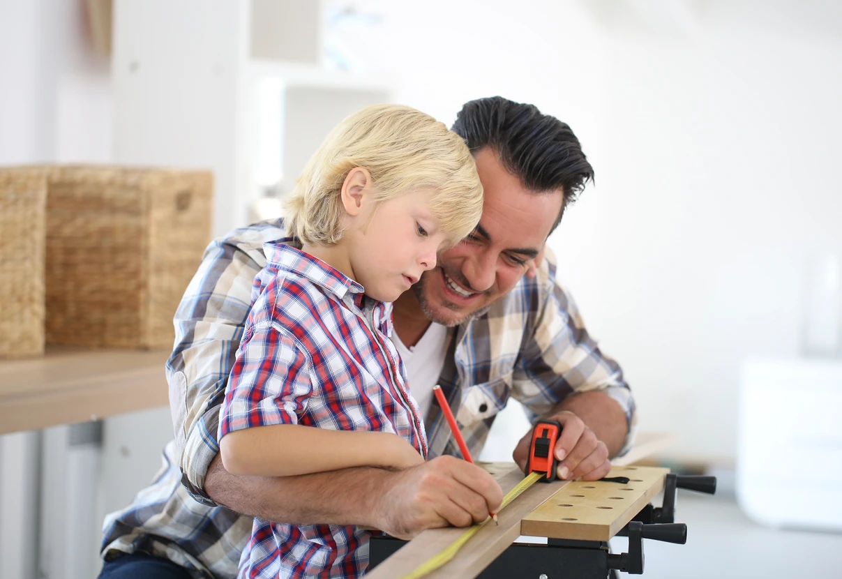 Père et fils travaillent ensemble dans un atelier de menuiserie, mesurant et marquant une planche en bois avec un crayon