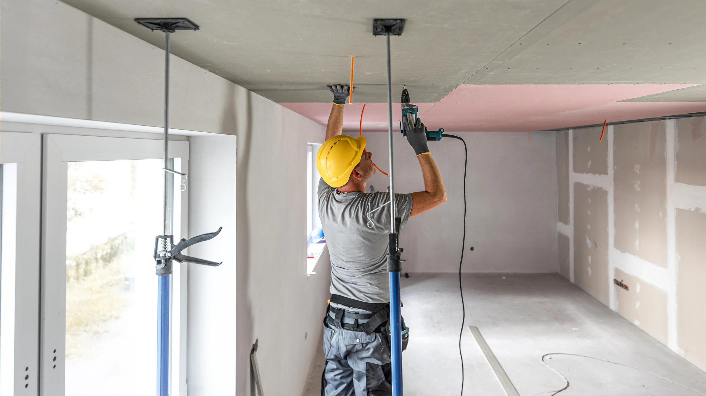 Photographie d'un artisan plâtrier professionnel, vêtu d'une tenue adaptée et équipé d'outils, en train de poser avec précision une plaque de plâtre sur une cloison intérieure dans un intérieur résidentiel en construction ou rénovation. L'image doit montrer le savoir-faire technique, la précision du travail et un environnement de chantier propre et organisé. Lumière naturelle ou professionnelle, composition dynamique mettant en avant le travail de qualité.