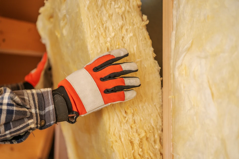 Vue arrière d'un contremaître dans des couloirs travaillant avec du matériel d'isolation en laine de roche, fixer la couche de chaleur sur le plafond et le mur, se tenant à l'intérieur d'une nouvelle maison en construction