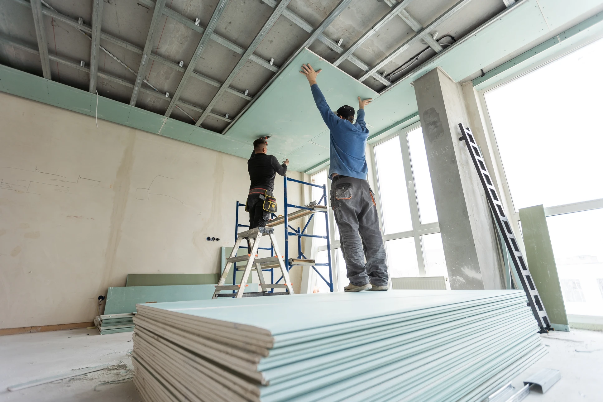 Une personne effectue des travaux de finition au plafond dans un intérieur, appliquant de l'enduit ou du plâtre avec un couteau à enduire